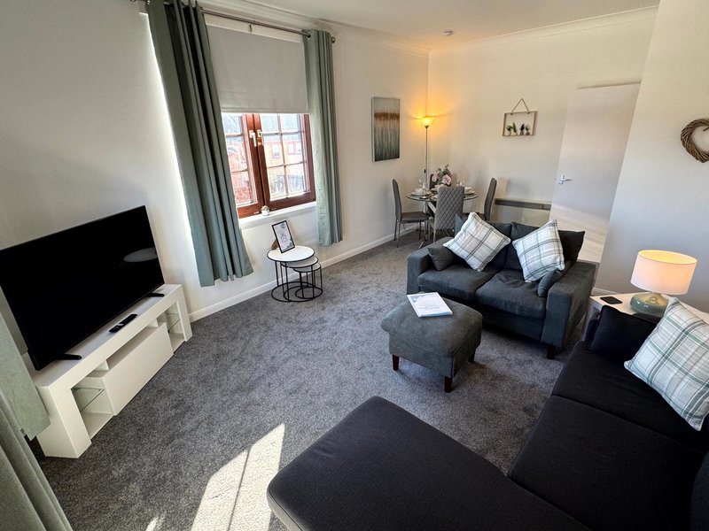 Modern living room with black sofas, TV, patterned cushions and grey carpet