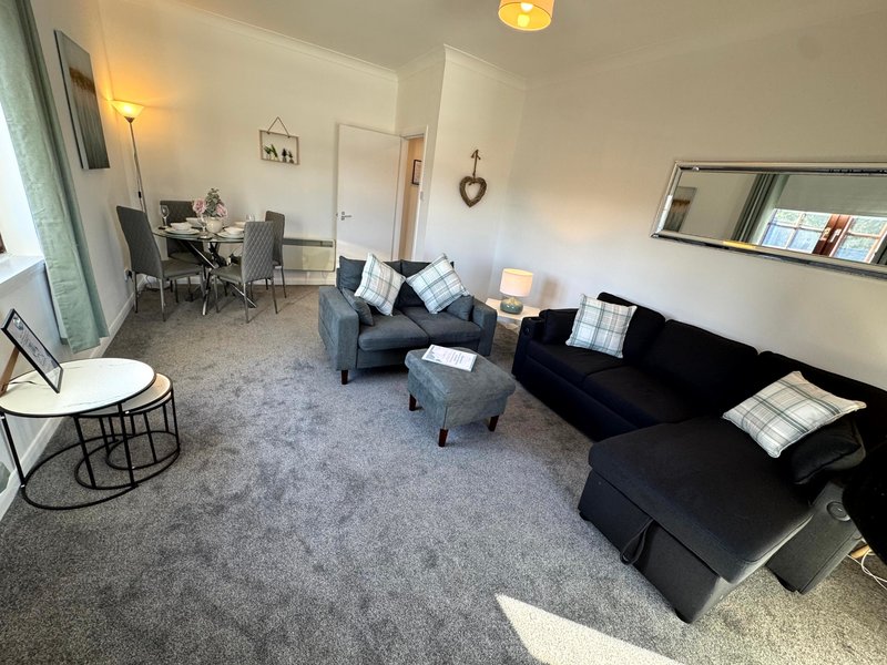 Open-plan living room with grey sofa, armchair, dining table and kitchen area