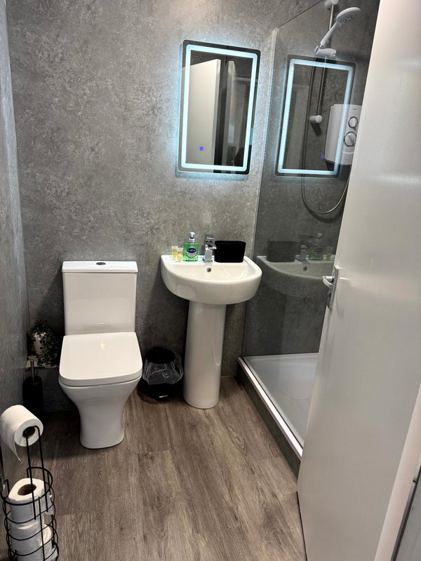 Modern bathroom with toilet, pedestal sink, illuminated mirrors and shower enclosure