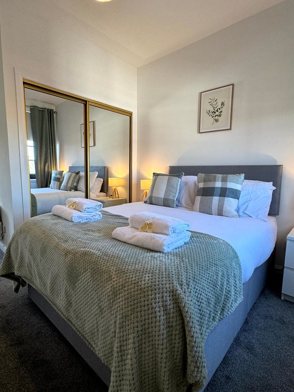 Modern bedroom with double bed, mirrored wardrobe, bedside lamps and framed wall art