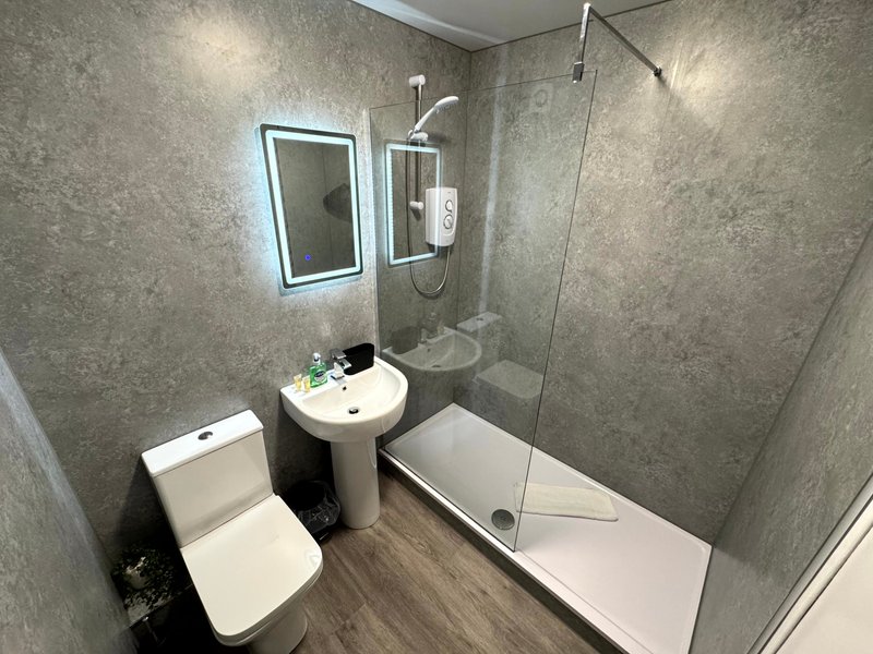 Modern bathroom with toilet, pedestal sink, illuminated mirror and walk-in shower