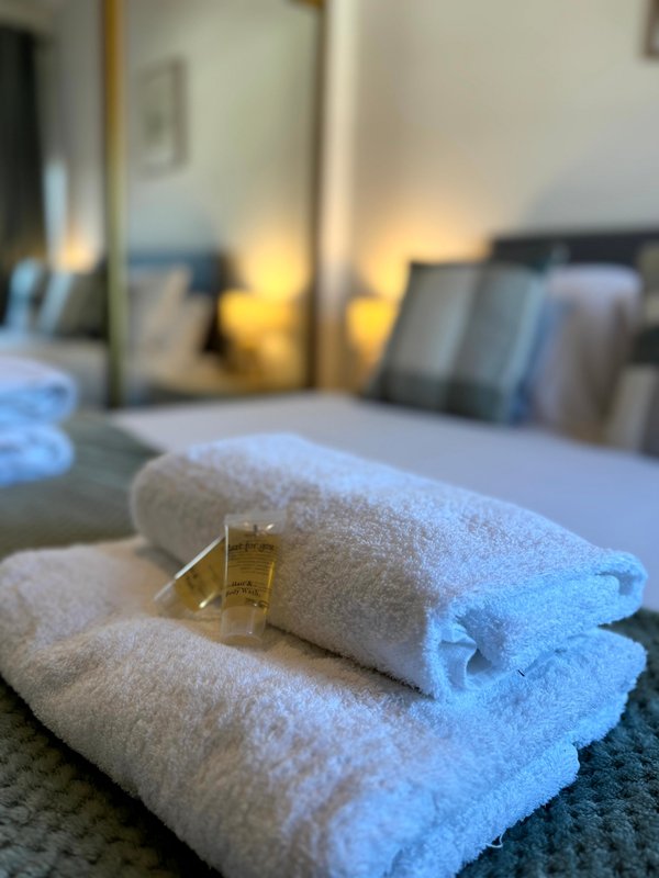 Rolled white towels with toiletries on bed, mirrored wardrobe in background
