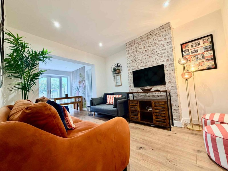 Modern living room with orange sofa, TV on brick wall, wooden floor and potted plant