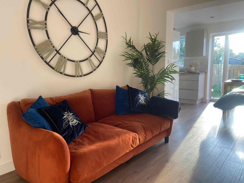 Spacious living room with rust-orange sofa, large wall clock, potted plant and glass doors to garden