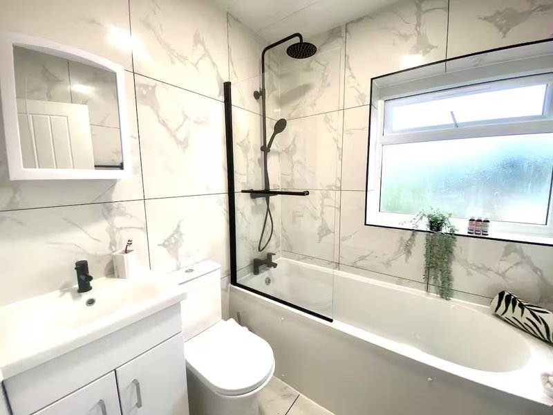 Modern bathroom with marble tiles, white sink, toilet, bathtub and black shower fixtures