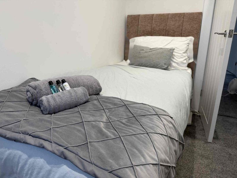 Bedroom with two single beds, gray bedding, cushions and pillows, brown headboard