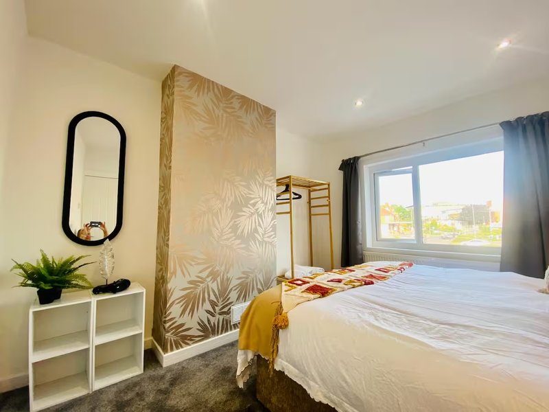 Modern bedroom with double bed, patterned headboard, white storage, black mirror and window