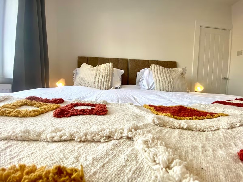 Bedroom with double bed, cream bedding, decorative red and gold throws, wooden headboard
