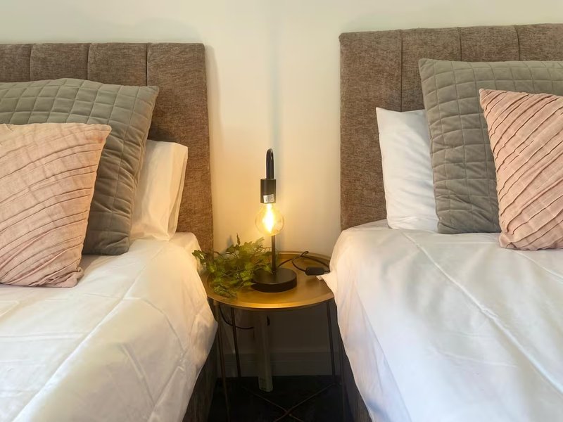 Twin bedroom with two beds, upholstered headboards, decorative pillows and bedside lamp