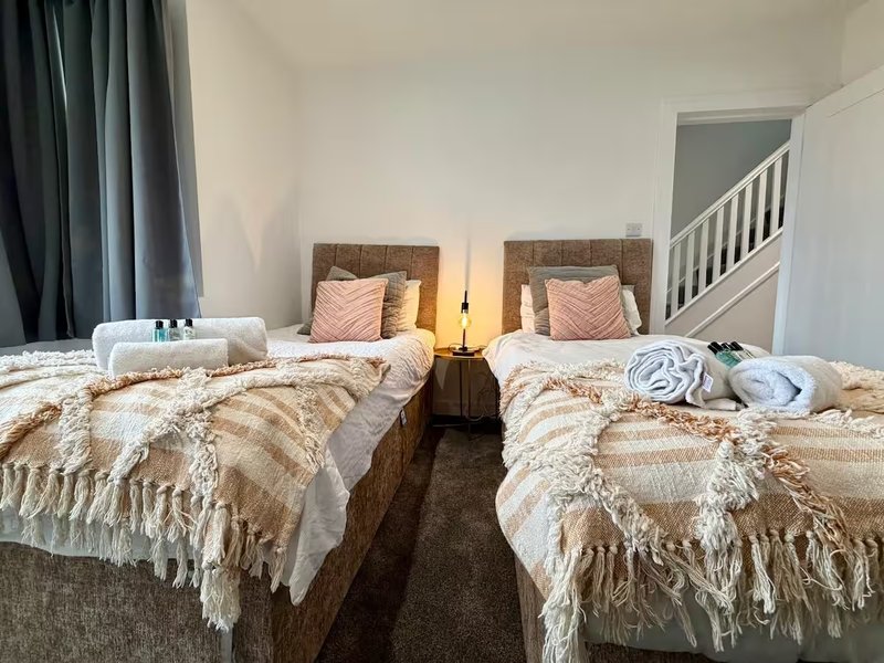 Twin bedroom with two single beds, wooden headboards, throws, and staircase visible