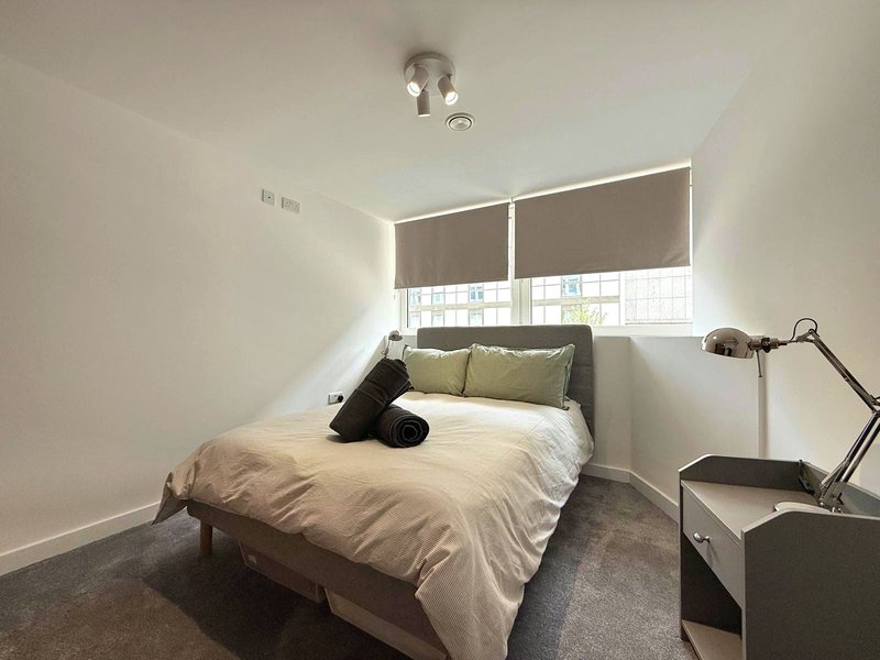 Modern bedroom with double bed, grey carpet, roller blinds and bedside lamp