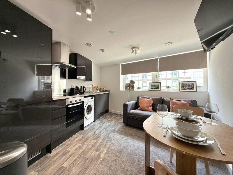 Open-plan kitchen and living area with black cabinetry, sofa, dining table and windows