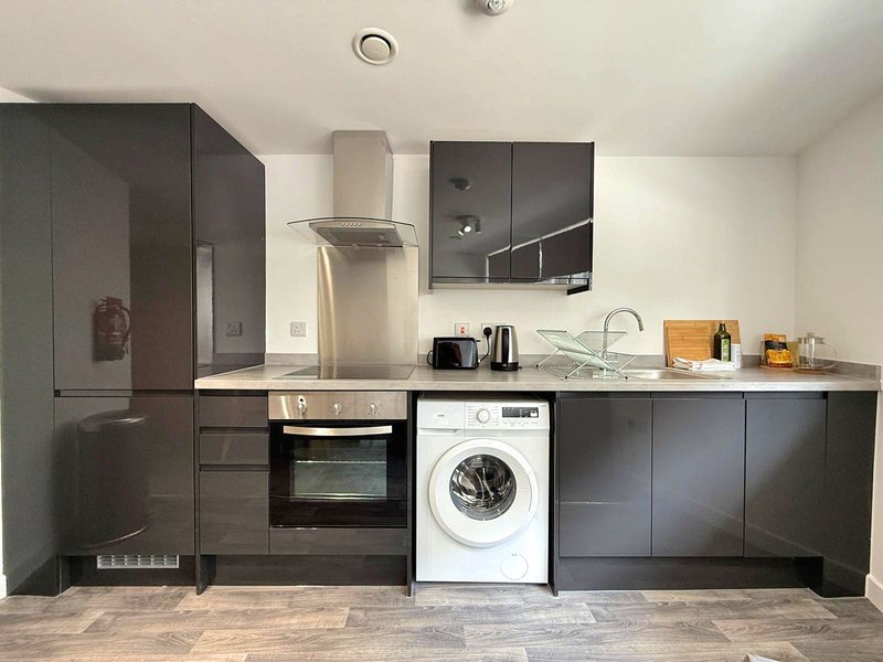 Modern kitchen with dark cabinetry, stainless steel appliances, washing machine and tiled flooring