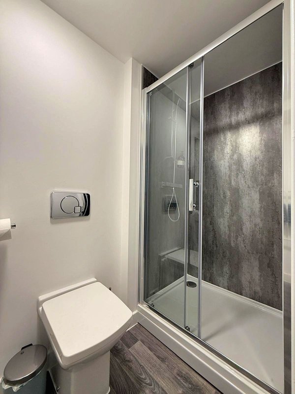 Modern bathroom with white toilet, glass shower enclosure and dark tiled walls