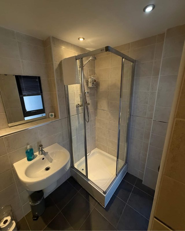 Modern bathroom with corner shower enclosure, white sink, and tiled walls