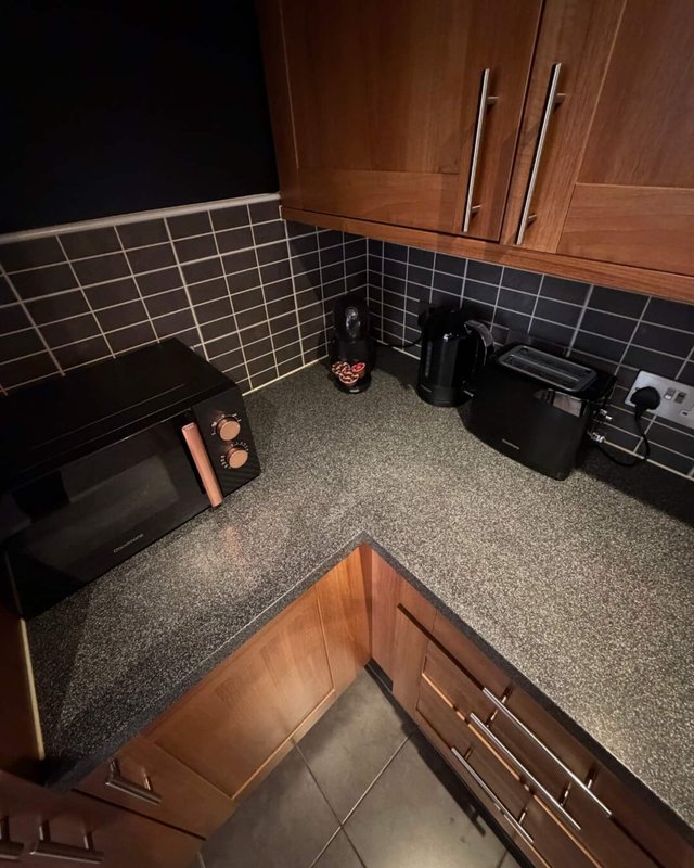 Kitchen corner with black tile backsplash, wooden cabinets, countertop appliances and utensils