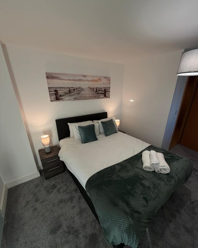 Modern bedroom with double bed, bedside lamps, framed artwork and grey carpet flooring