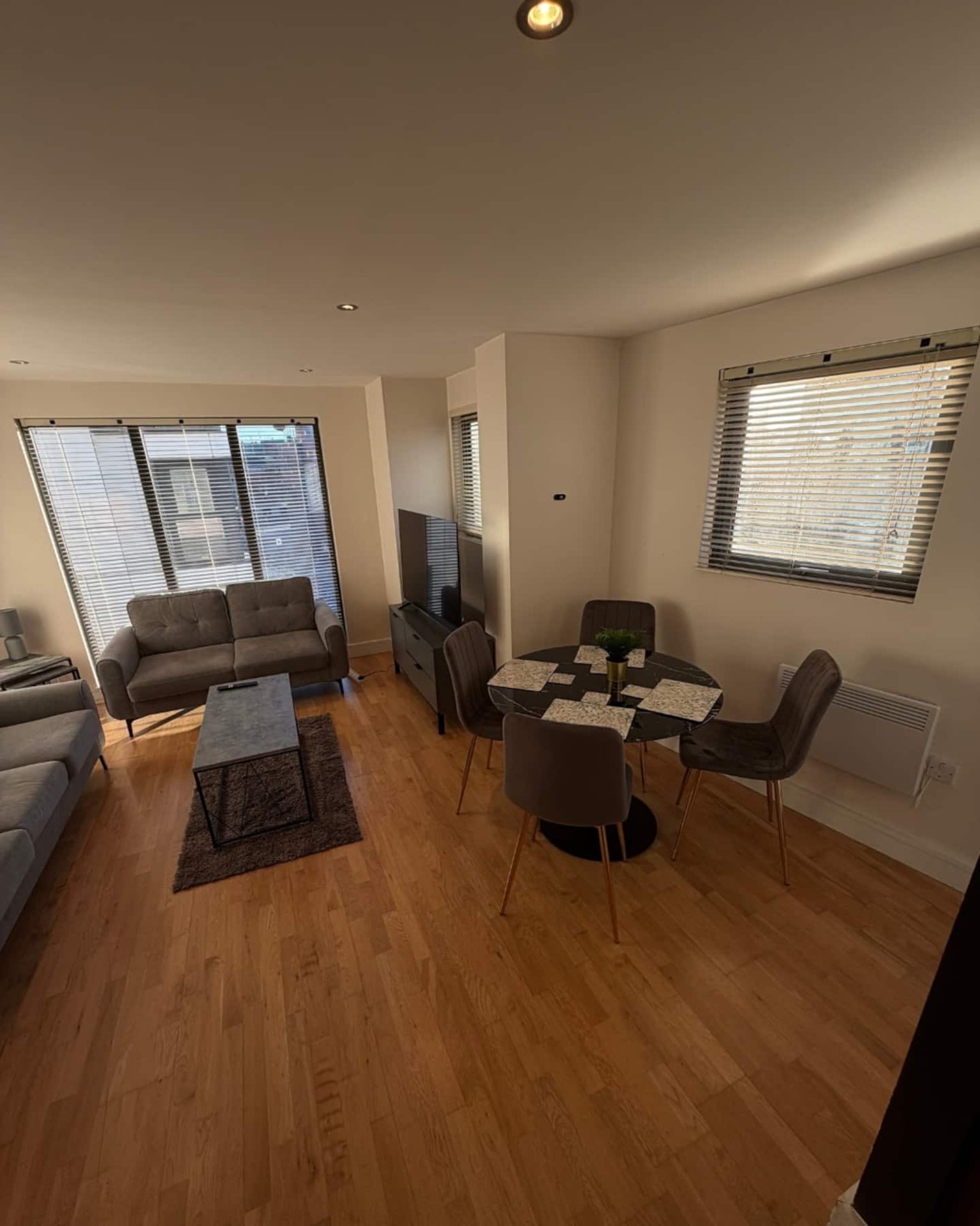 Open-plan living room with dining table, sofa, wooden flooring and large windows
