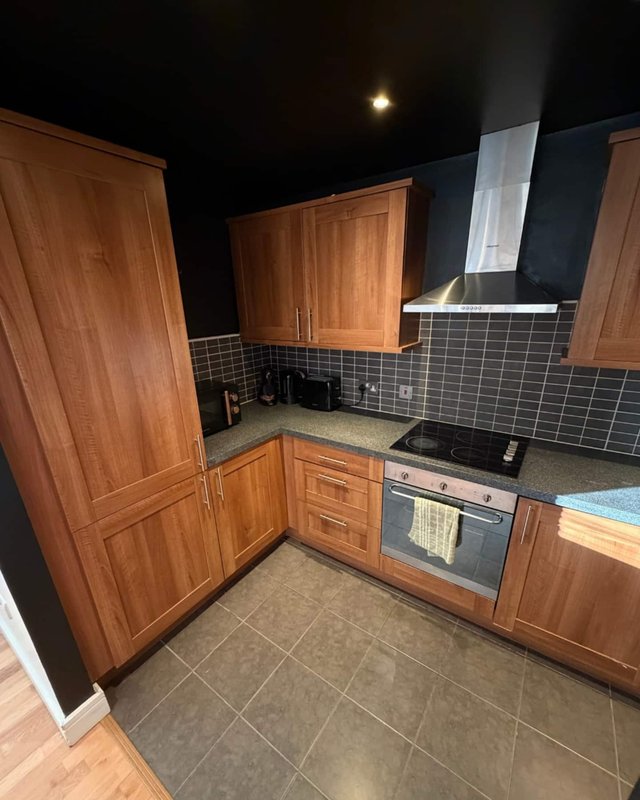 Modern kitchen with wooden cabinets, black tile backsplash, stainless steel range hood and built-in oven