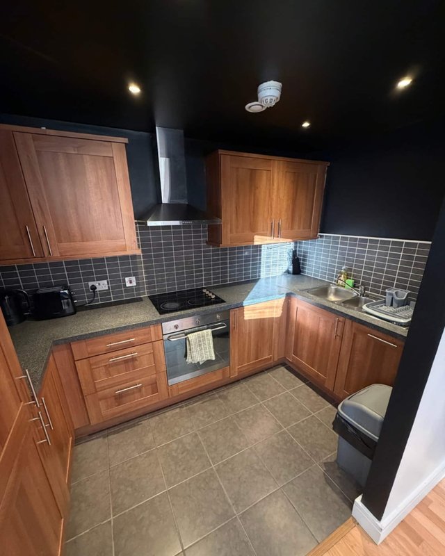 Modern kitchen with wooden cabinets, dark tile backsplash, stainless steel appliances and dark ceiling