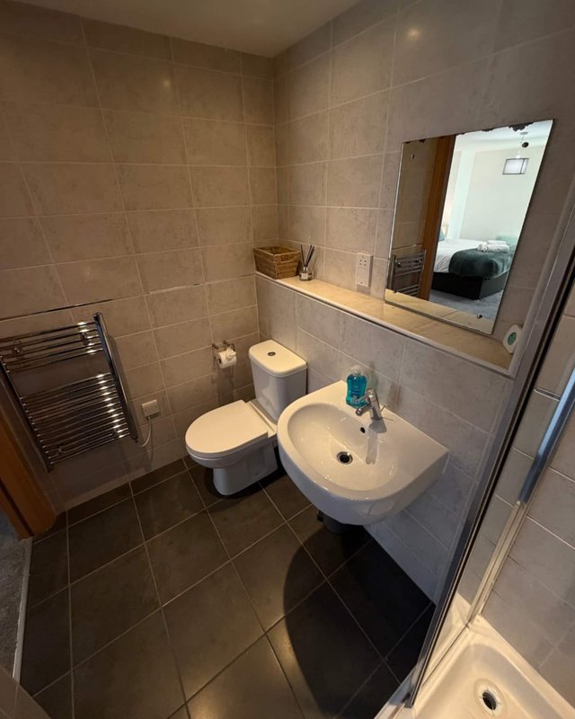 Bathroom with toilet, pedestal sink, mirror, towel rail and tiled walls