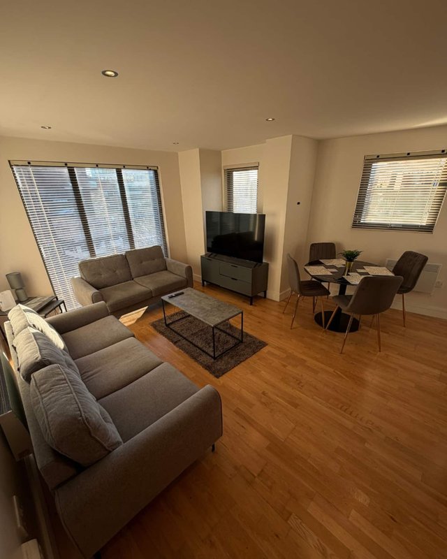 Spacious living room with grey sofas, wooden floor, TV, and large windows