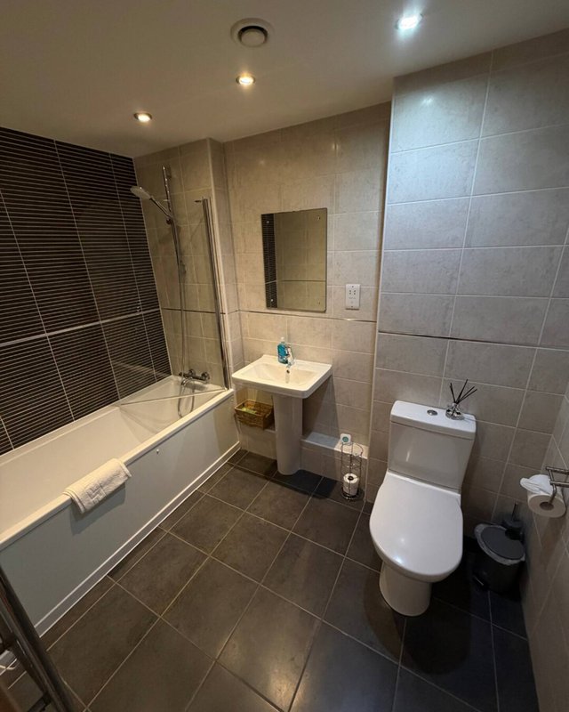Modern bathroom with bathtub, toilet, sink, mirror and tiled walls