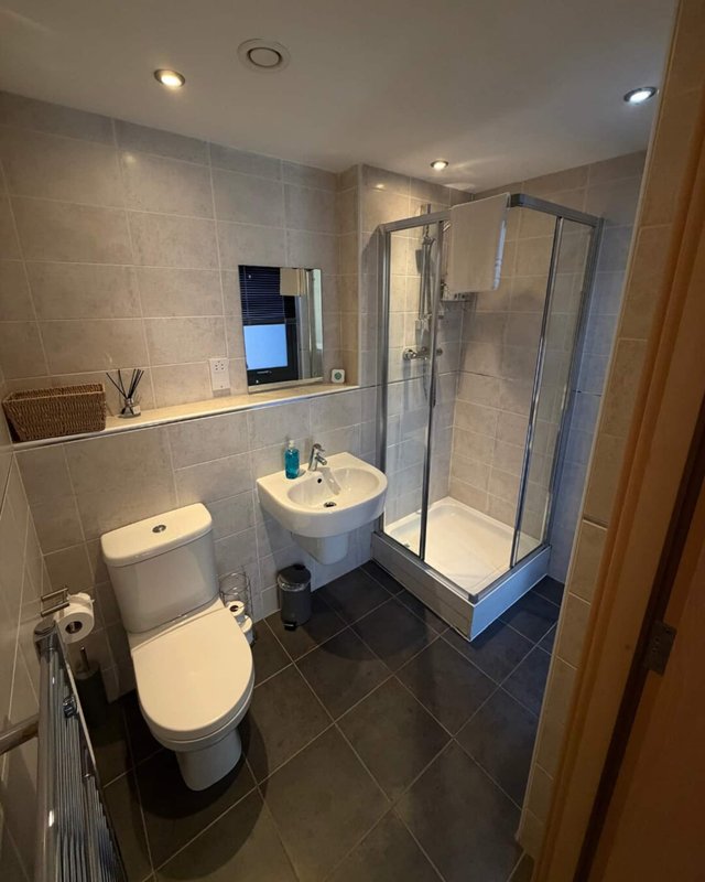 Modern bathroom with toilet, pedestal sink, shower enclosure and tiled walls