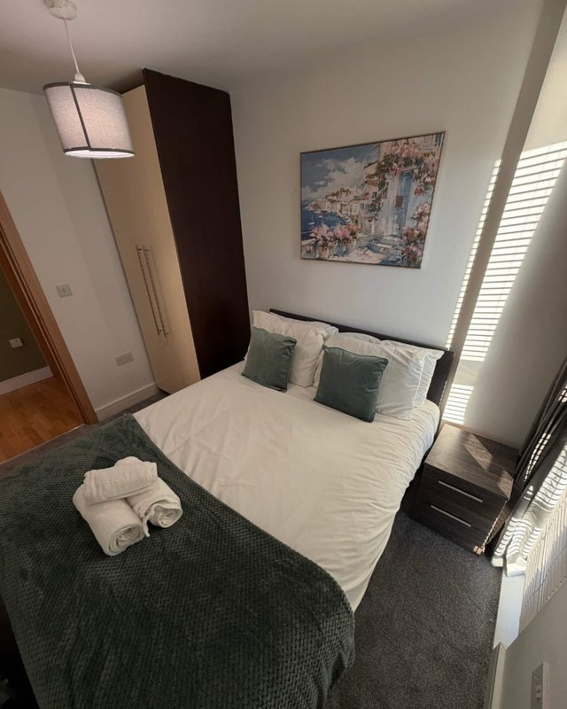 Bedroom with double bed, green bedding, white pillows, framed artwork, and wooden flooring