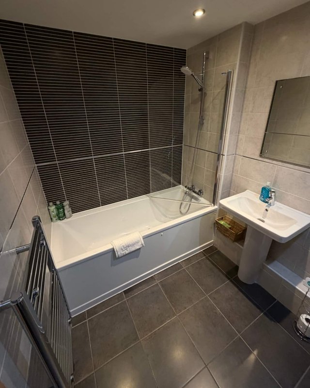 Modern bathroom with bathtub, black tile shower screen, pedestal sink and mirror