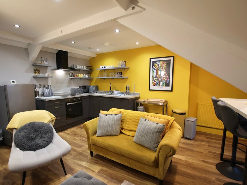 Open-plan kitchen and living area with yellow walls, black cabinetry, yellow sofa and wooden flooring