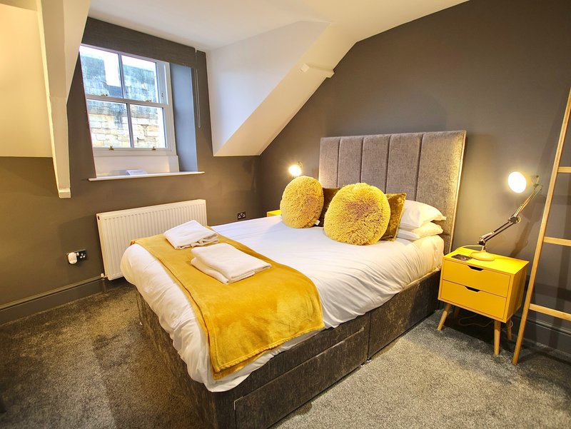 Modern bedroom with double bed, yellow bedding, upholstered headboard and matching nightstand