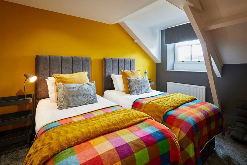 Twin bedroom with grey upholstered headboards, colorful quilts, and bright yellow walls under sloped ceiling