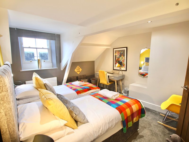 Bright bedroom with two single beds, colorful blankets, yellow accents, desk and window view