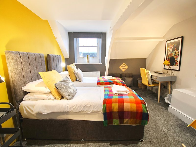 Bright bedroom with double bed, yellow accent wall, colourful throw blanket and window