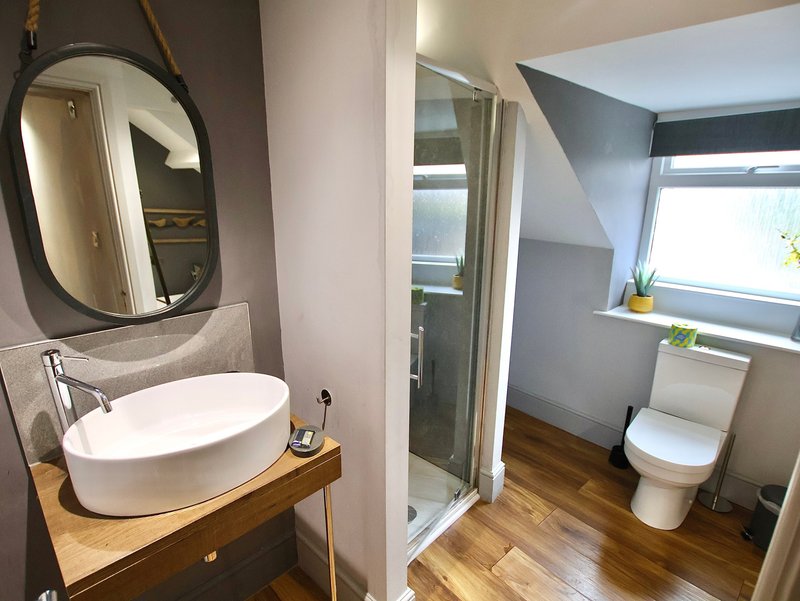 Modern bathroom with oval mirror, vessel sink, wooden vanity, shower enclosure and toilet