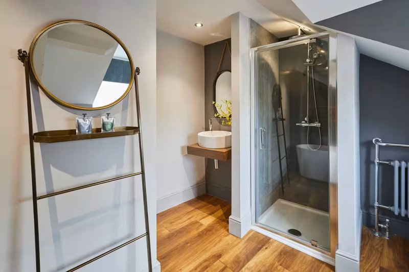 Modern bathroom with round mirror, wooden floor, sink, and glass shower enclosure