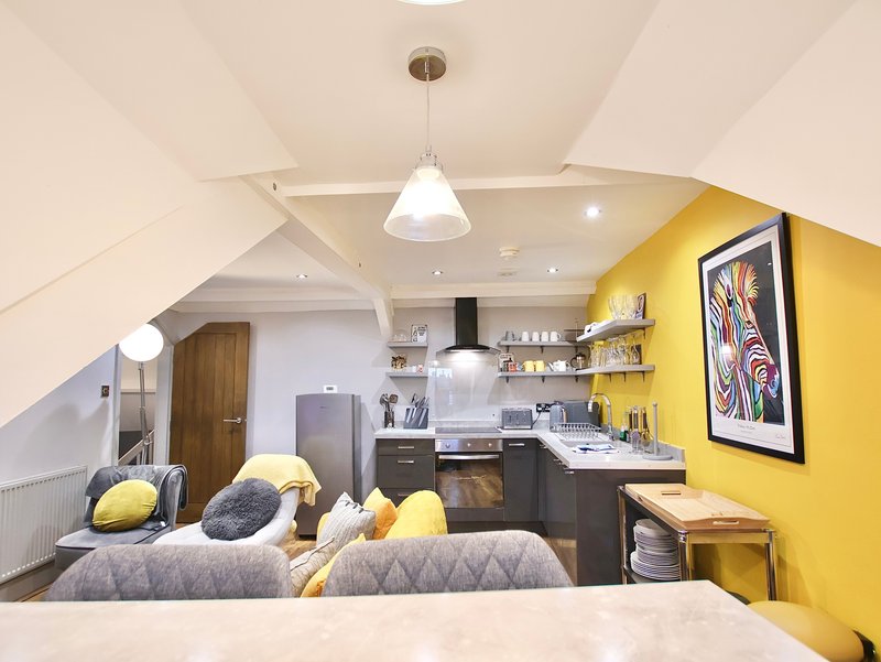 Open-plan studio with yellow accent wall, kitchenette, seating area and pendant lighting
