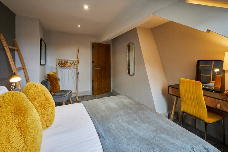 Modern bedroom with double bed, yellow cushions, wooden desk, and angled ceiling with warm lighting