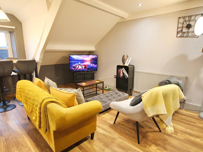Bright attic living room with yellow sofa, TV, white chair, wooden floors and wall clock