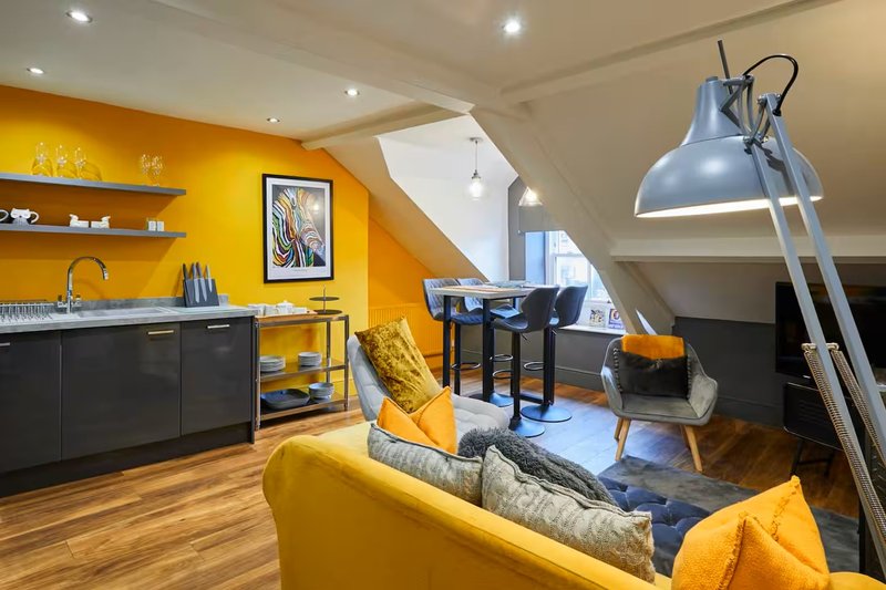Modern open-plan kitchen and living area with yellow accent wall, black cabinetry, wooden flooring and contemporary furnishings