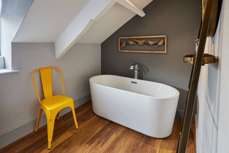 Modern bathroom with freestanding white bathtub, yellow metal chair, and wooden flooring