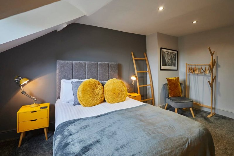 Modern bedroom with double bed, yellow cushions, grey headboard and wooden ladder decor