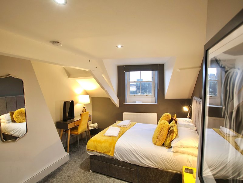 Modern bedroom with double bed, yellow bedding, desk chair, and sloped ceiling with window