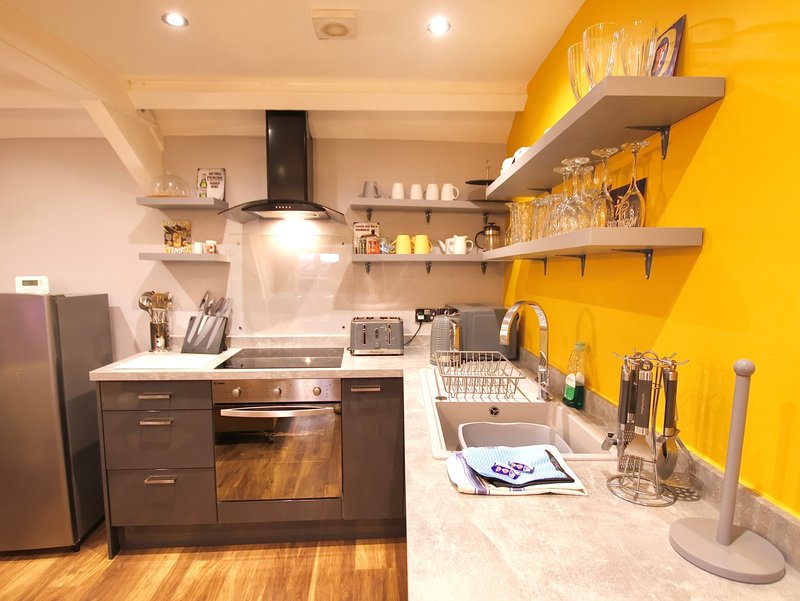 Modern kitchen with yellow accent wall, dark cabinetry, stainless steel appliances and open shelving