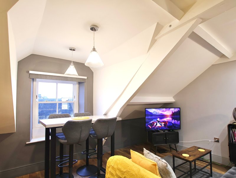 Loft bedroom with dining area, TV, yellow bedding, and sloped ceiling with pendant lights