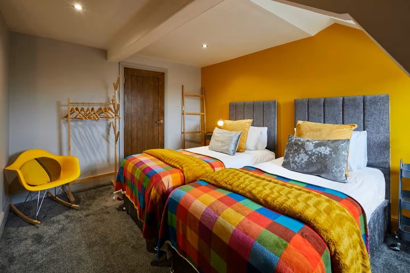 Modern bedroom with two beds, colorful quilts, yellow accent wall, and contemporary furnishings