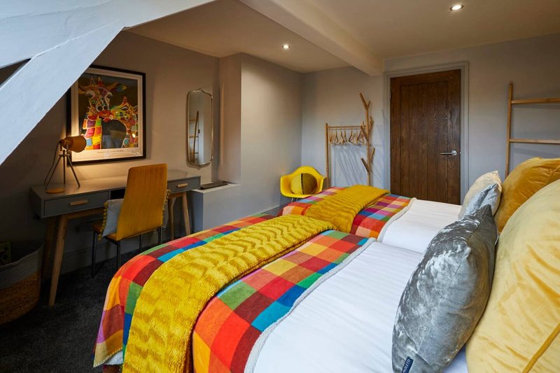 Bright attic bedroom with double bed, colorful quilt, desk, and wooden doors