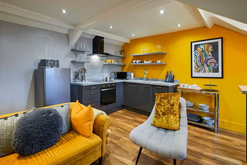 Open-plan kitchen and living area with yellow accent wall, dark cabinetry, and modern furnishings