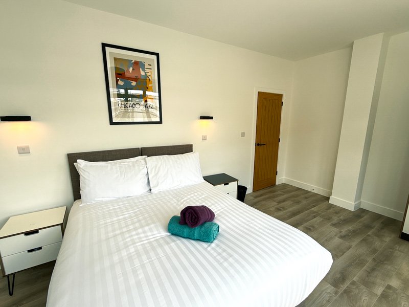 Bedroom with double bed, white bedding, dark headboard, wooden door and neutral walls